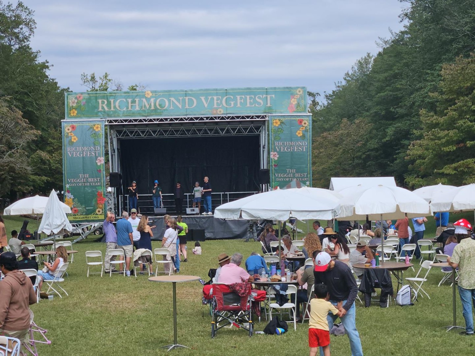 A main-stage gathering space with people sitting and moving through the festival lawn.